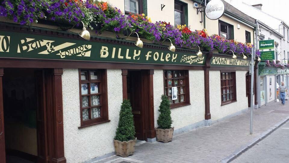 The green and gold shopfront of Billy Foley's Bar, with hanging baskets of flowers